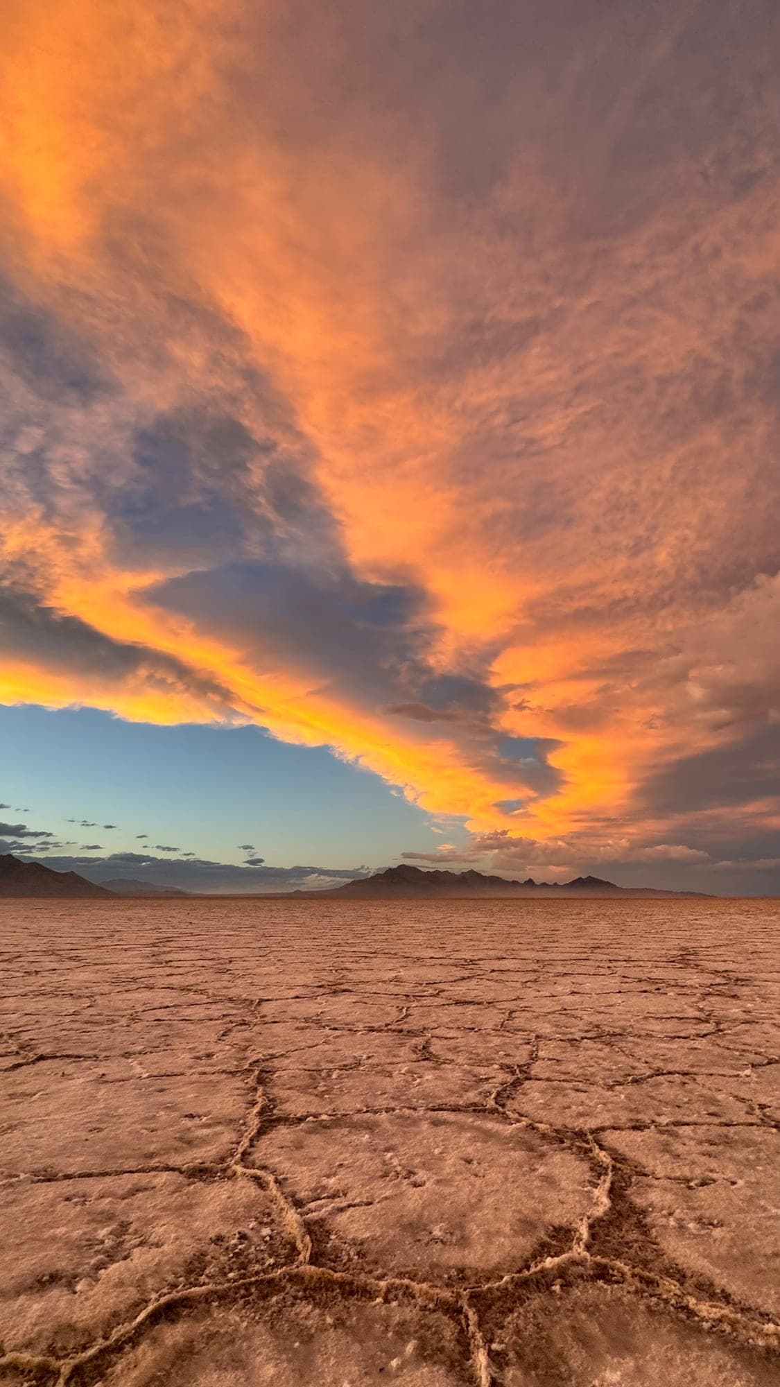 A fiery sunset sky over cracked desert ground