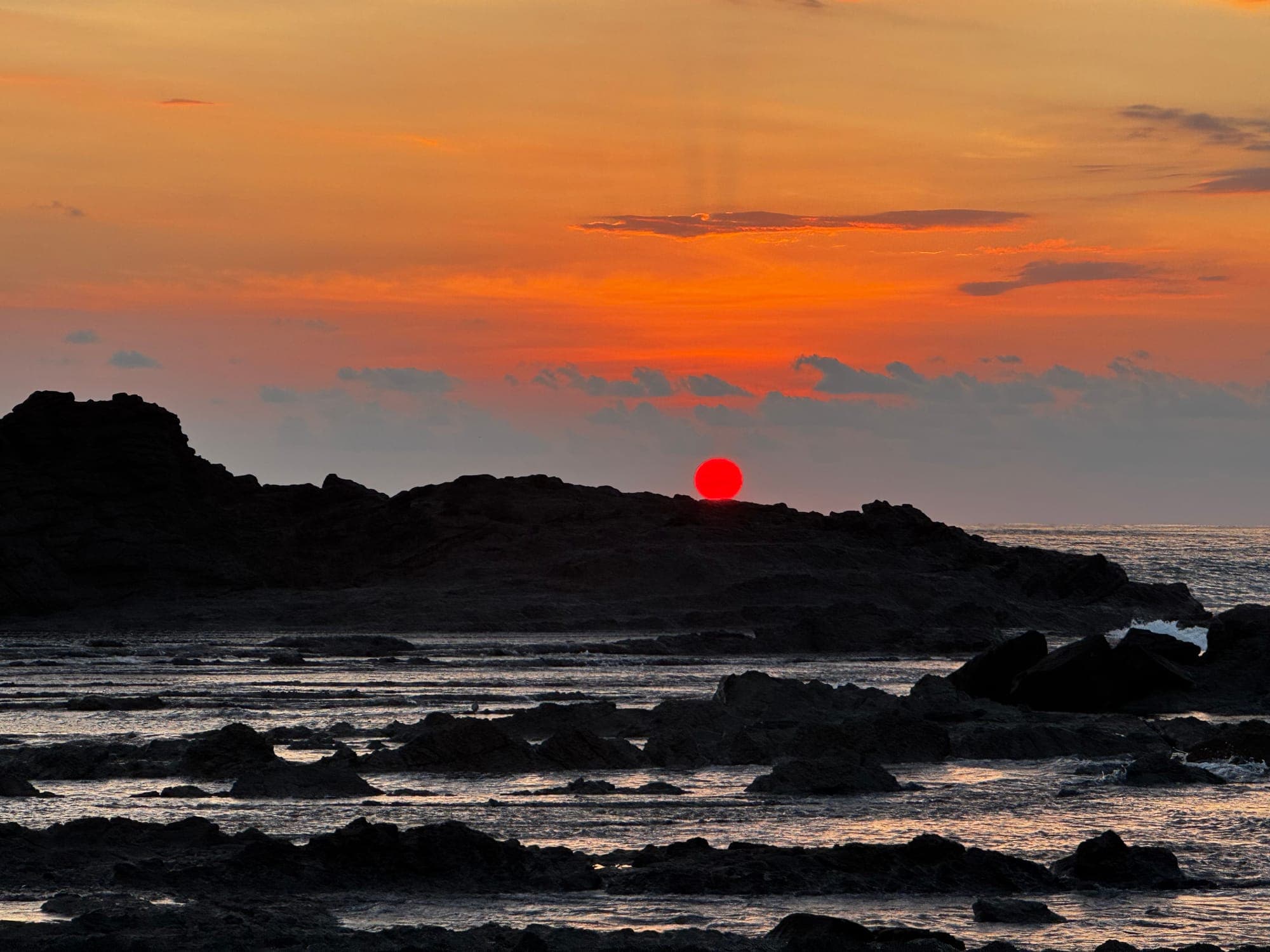 Black lava rock at the shoreline under a red setting sun