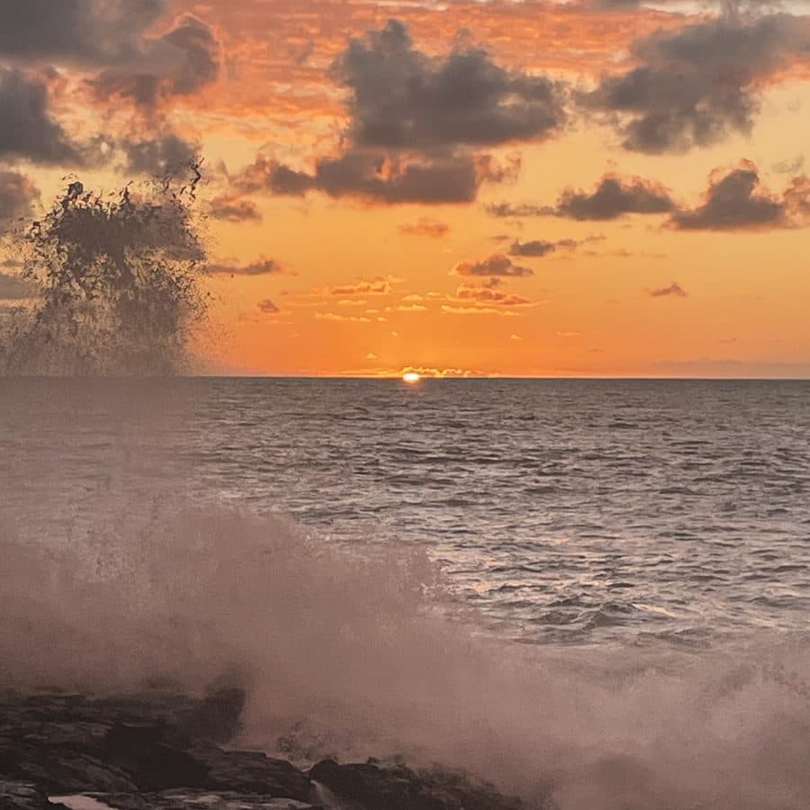 A wave crashing on the rocks as the sun sets over the sea