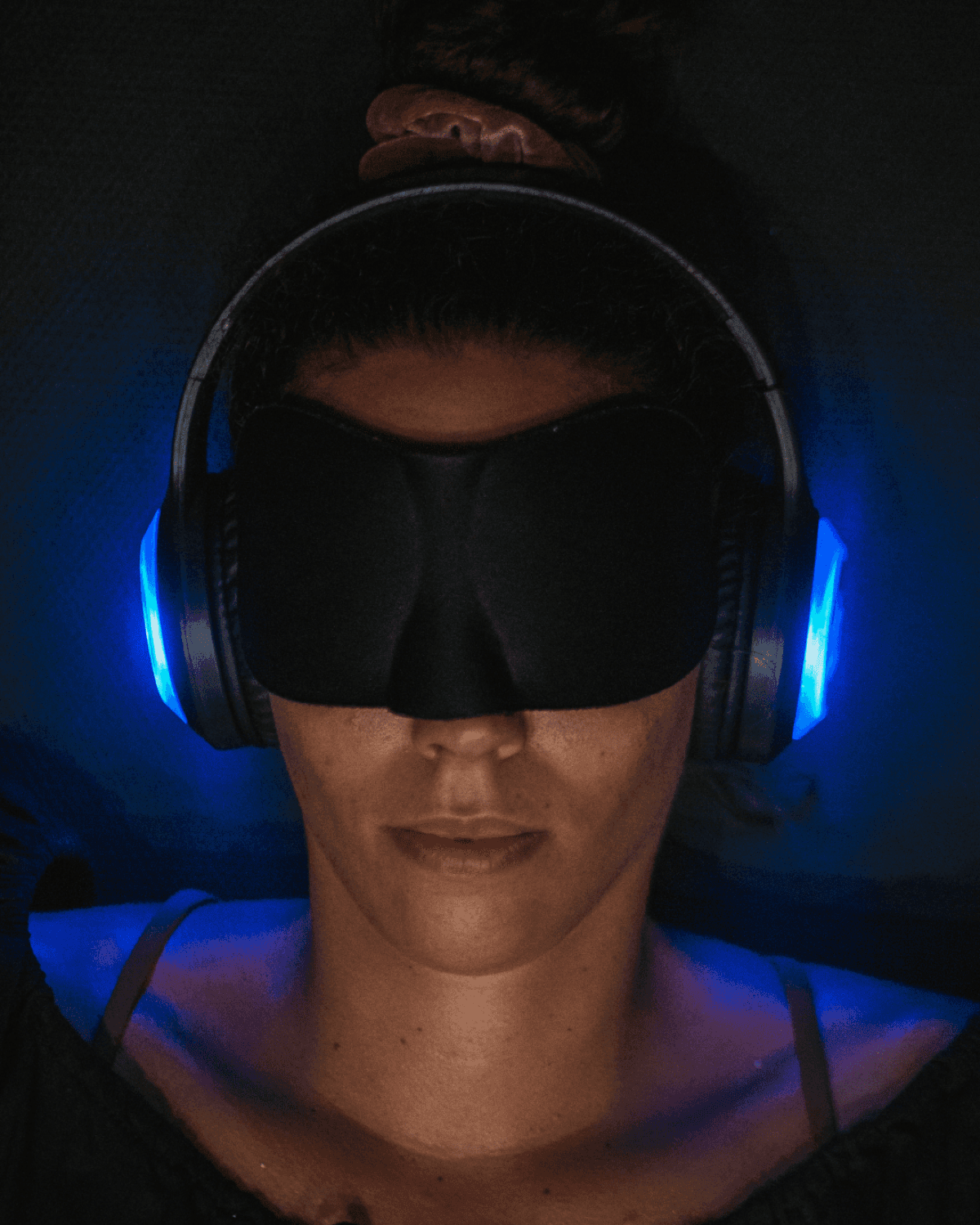 A woman resting in a 9D headset glowing blue, an eye mask over her eyes