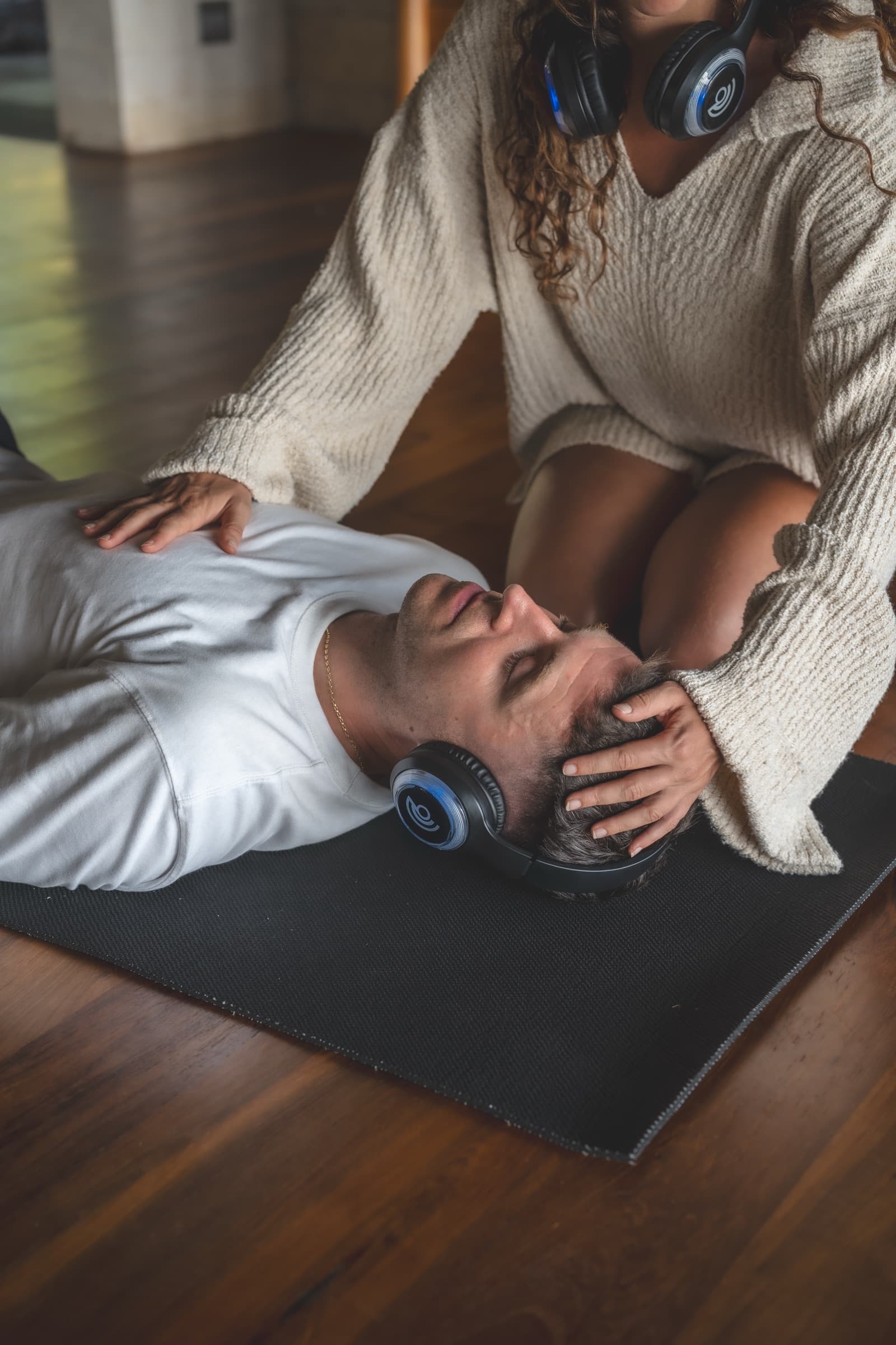 A practitioner's hands resting on the shoulders of a man lying in a headset