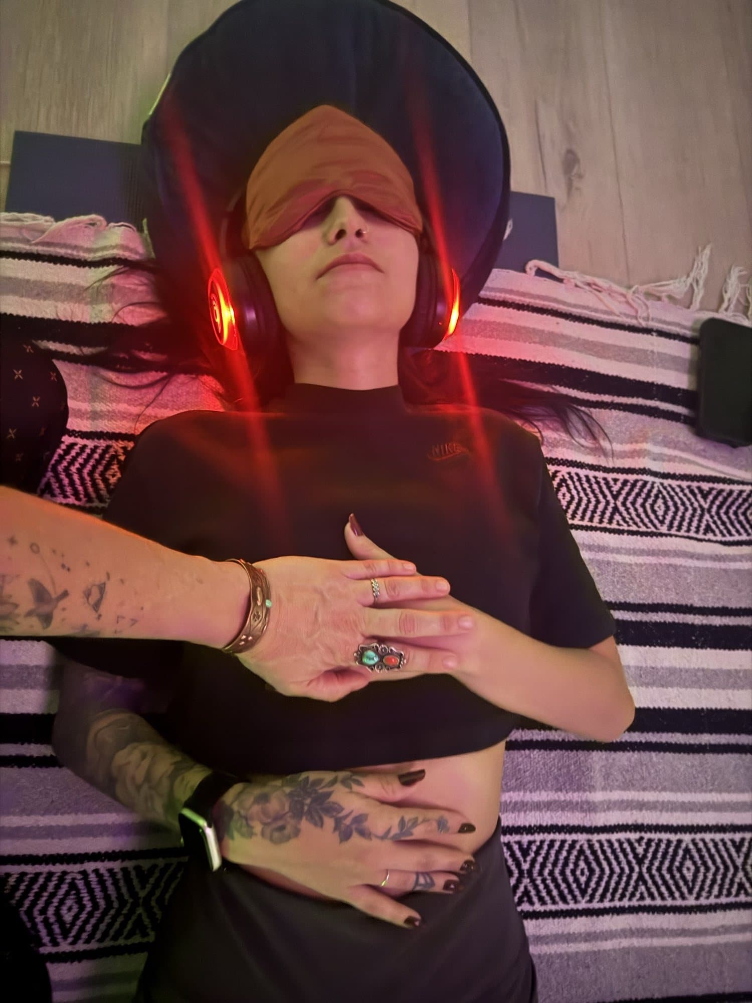 Someone resting in a glowing red headset and eye mask, hands over their heart and belly
