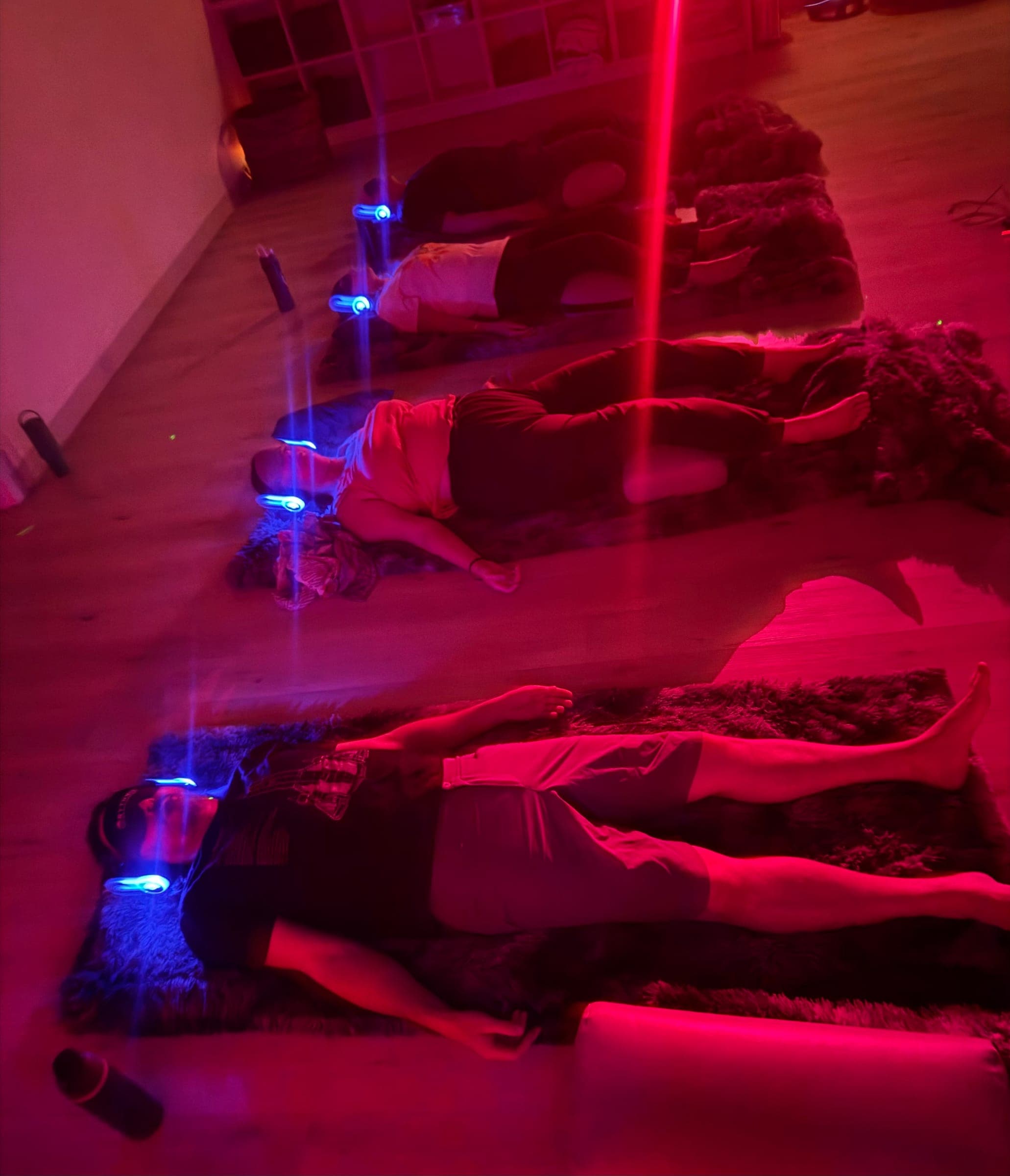 A group lying in rows on the floor in red light, blue lights glowing on their headsets