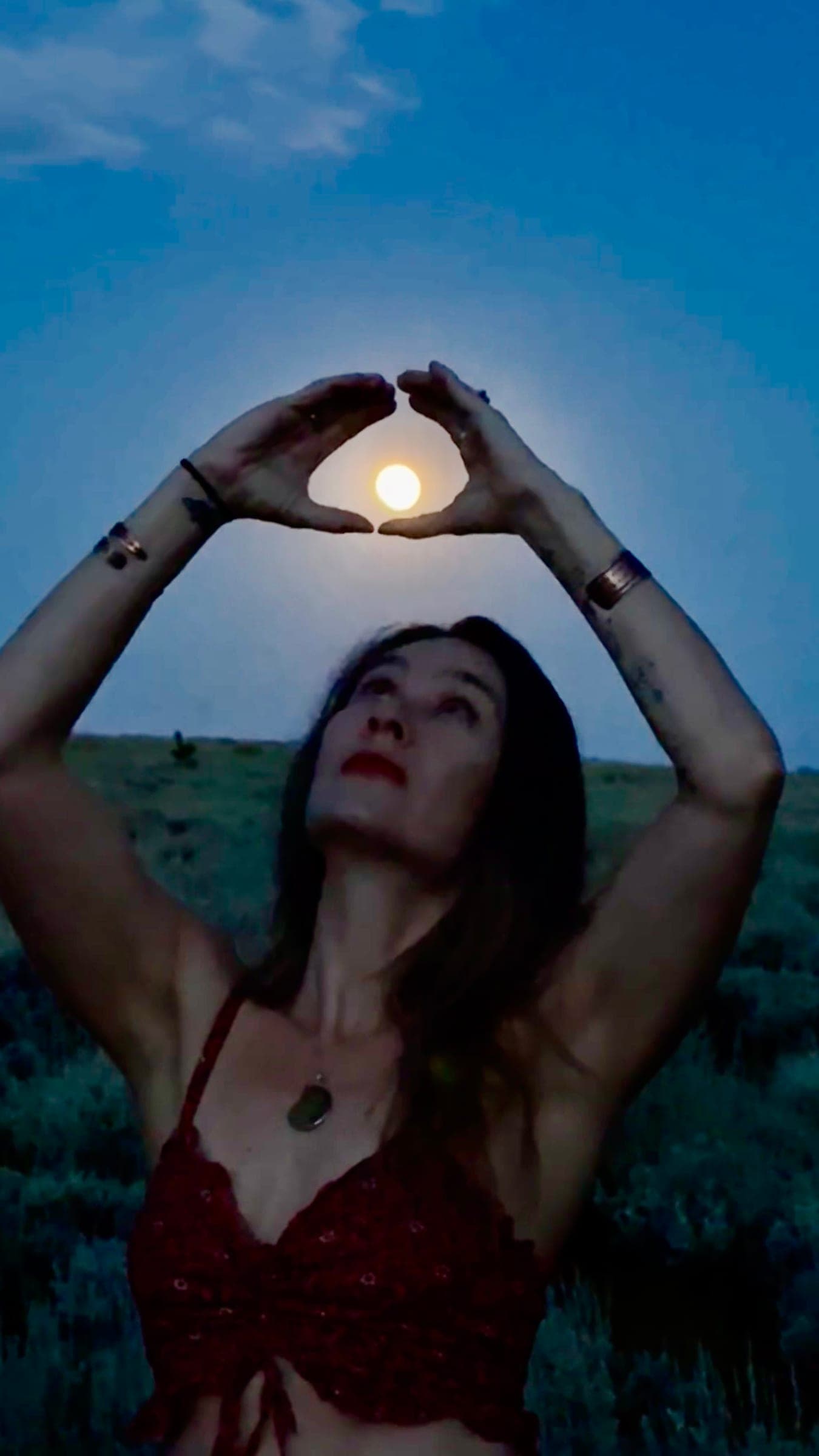Rachel at dusk with her hands raised in a triangle around the glowing moon