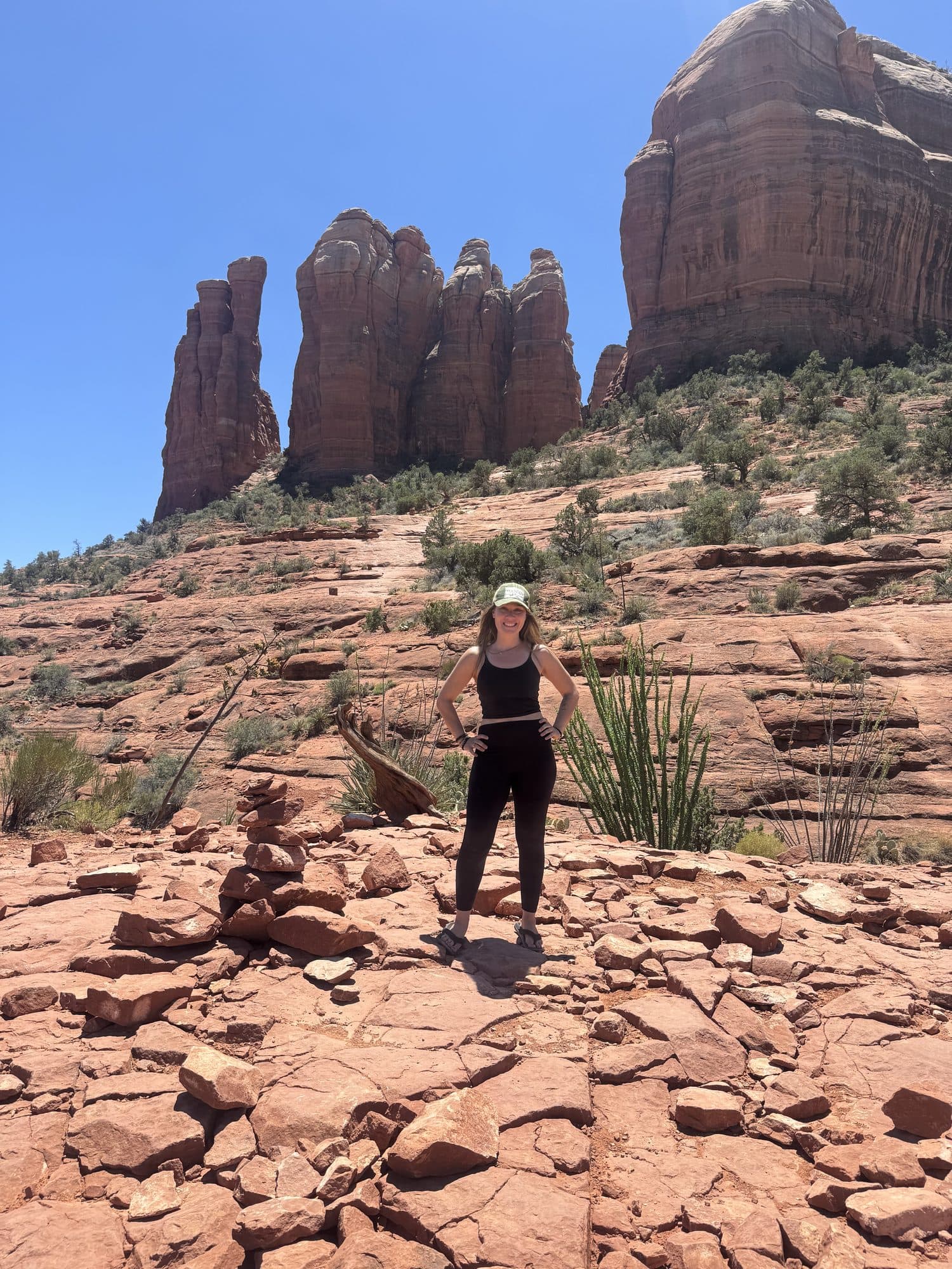 Rachel standing among red rocks, tall red spires rising behind her under a blue sky