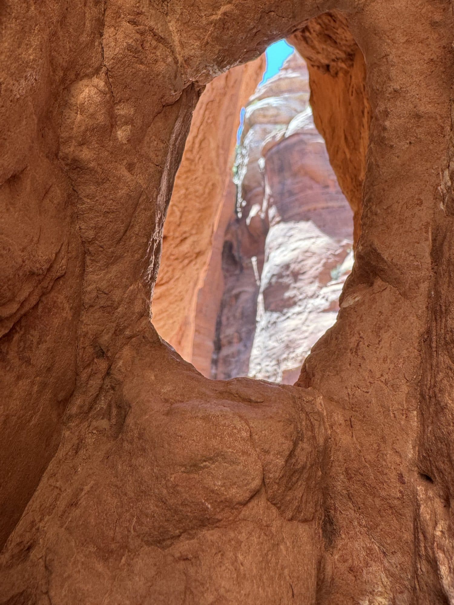 A window worn through red rock, blue sky showing through it