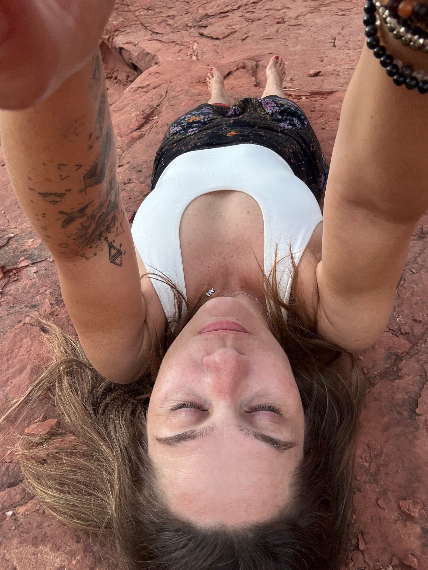 Rachel lying on red earth, eyes closed, arms open above her