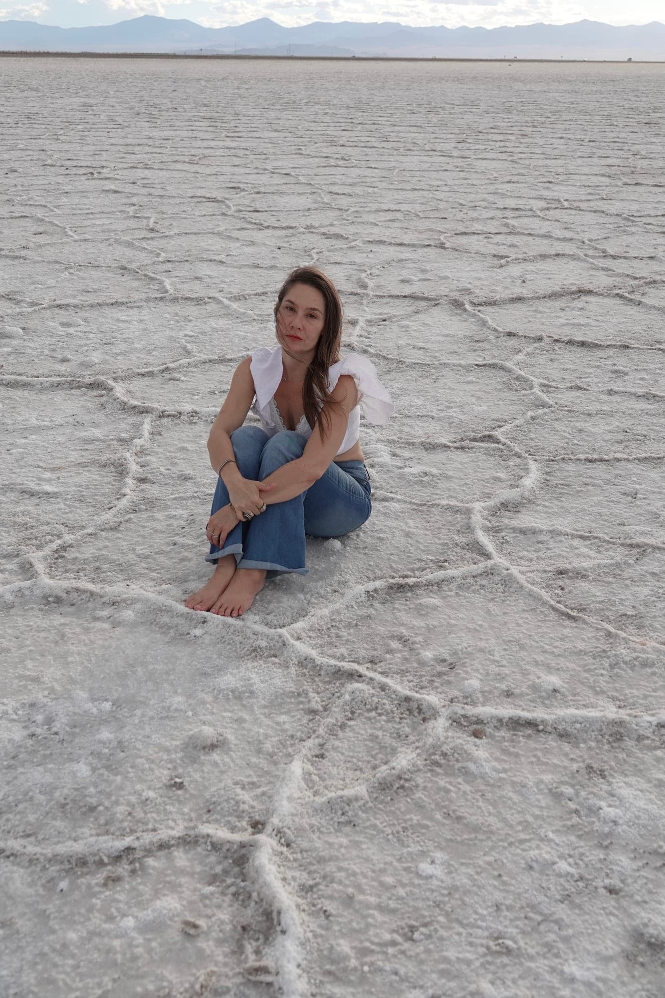 Rachel sitting barefoot on the white salt flats, the cracked ground spreading out around her
