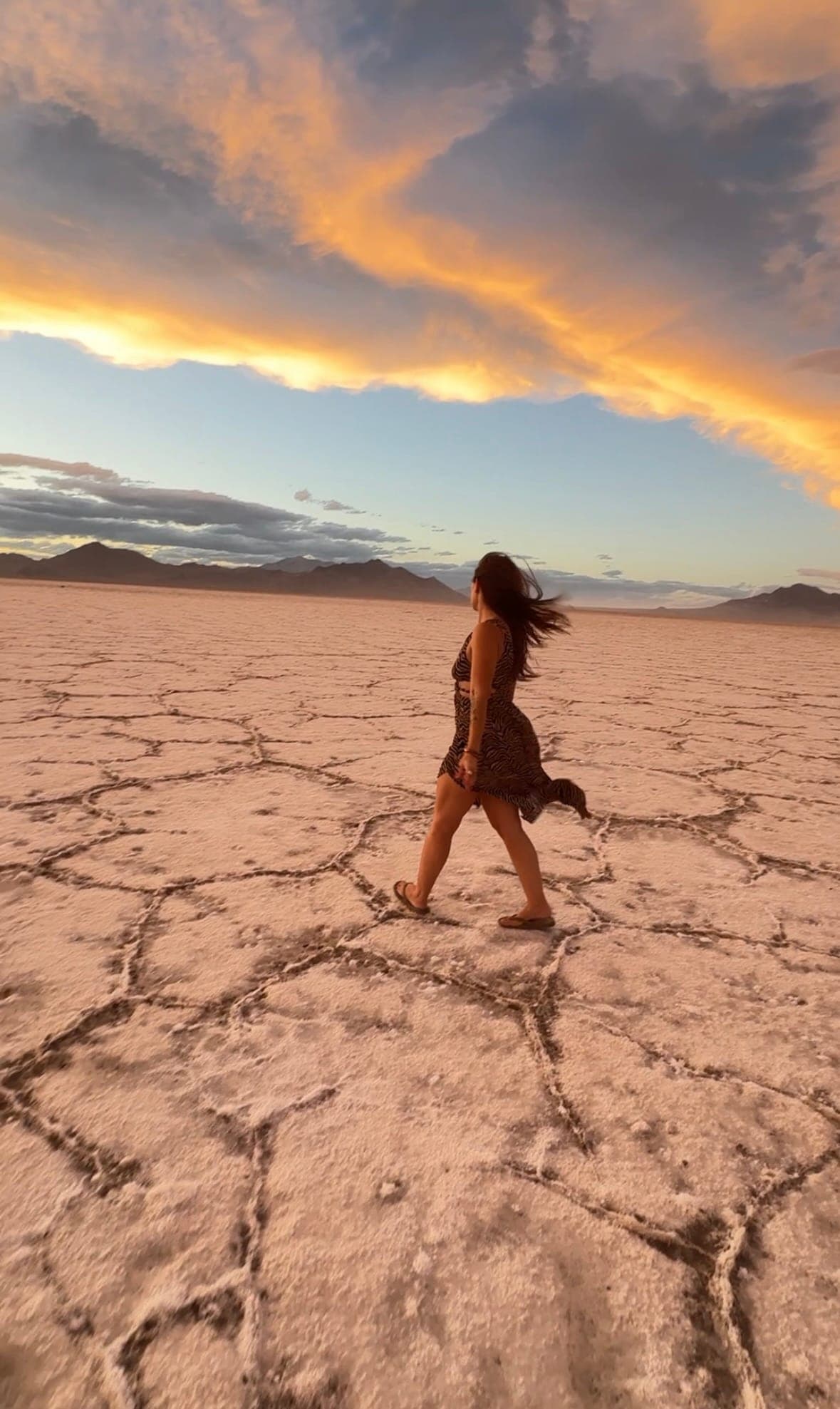 Rachel walking barefoot across cracked earth toward a fire-colored sunset sky
