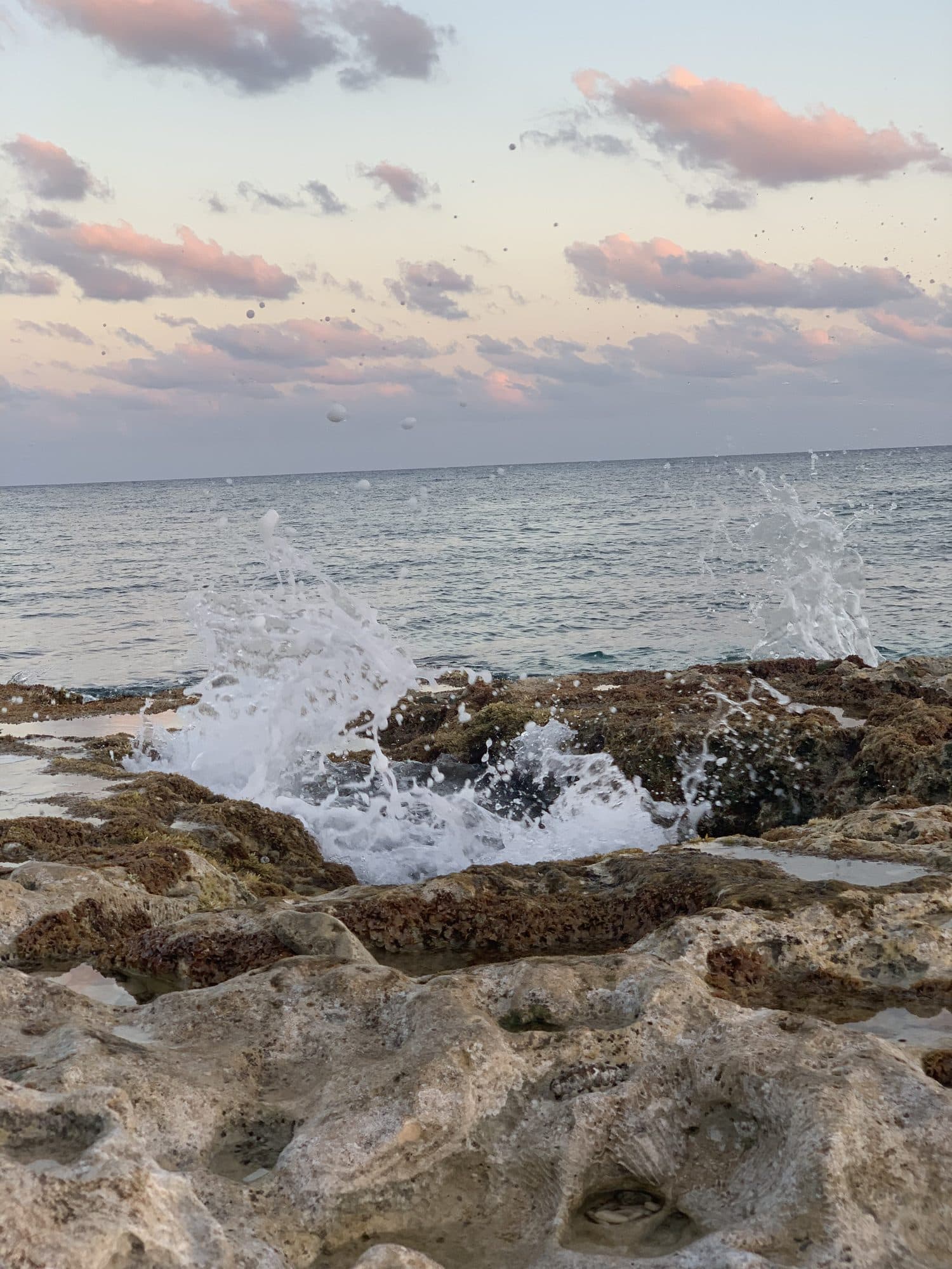 Waves bursting over the rocks under a soft pink sunset sky