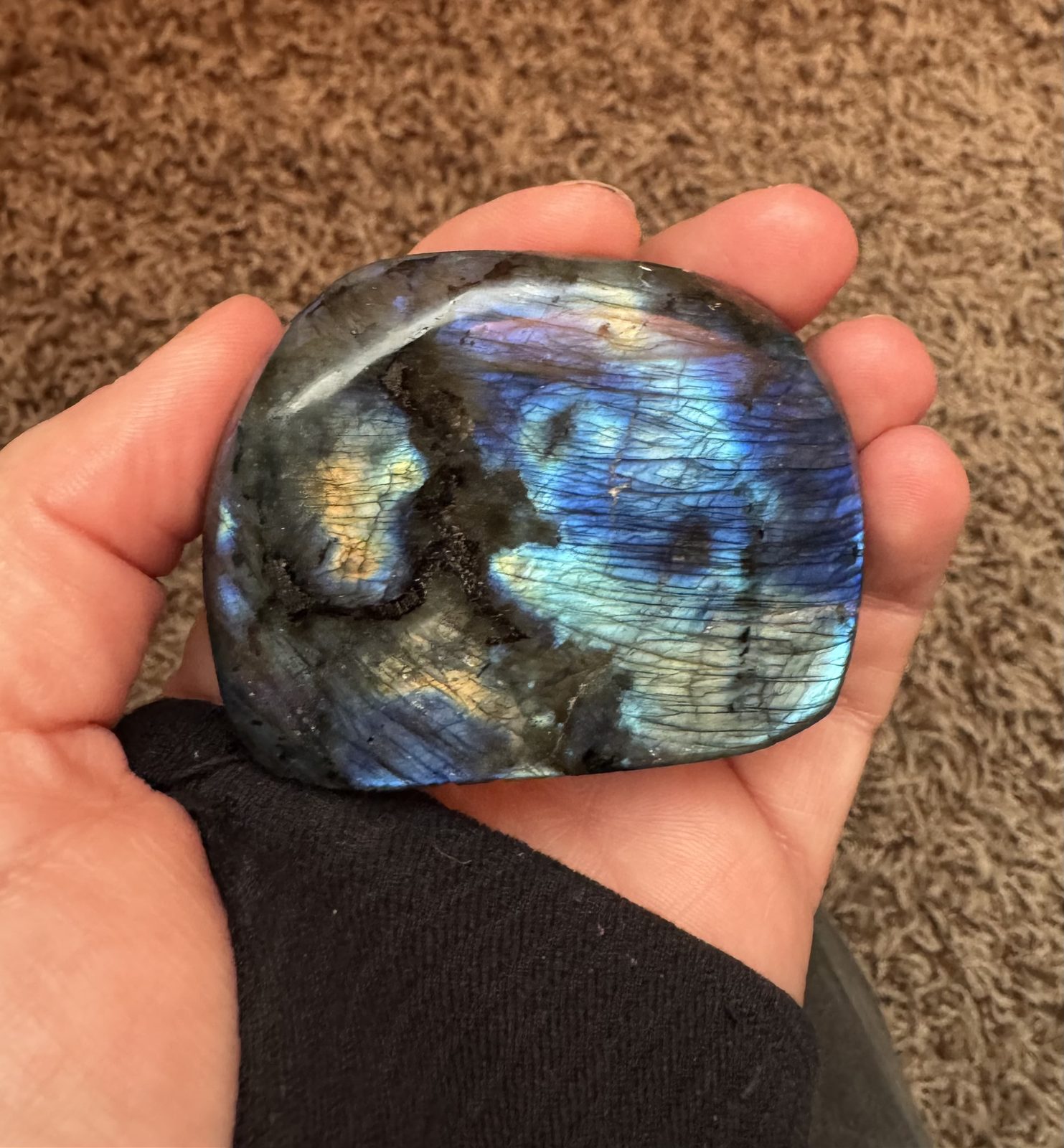 A polished piece of labradorite in an open hand, flashing blue and gold