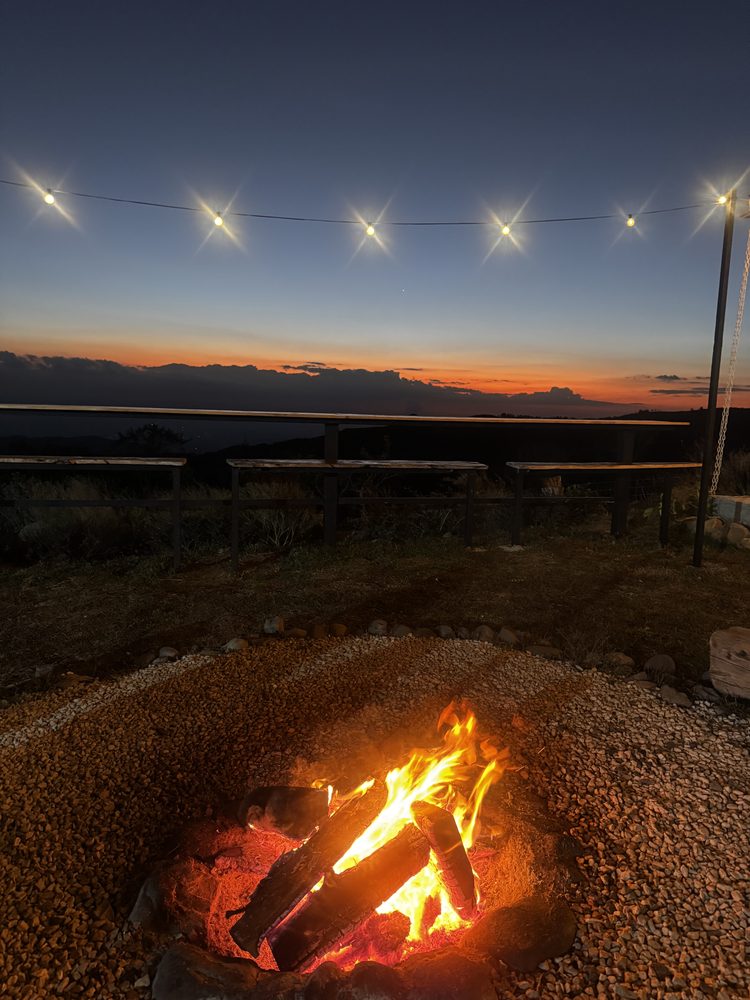 A fire pit burning at dusk under strings of lights