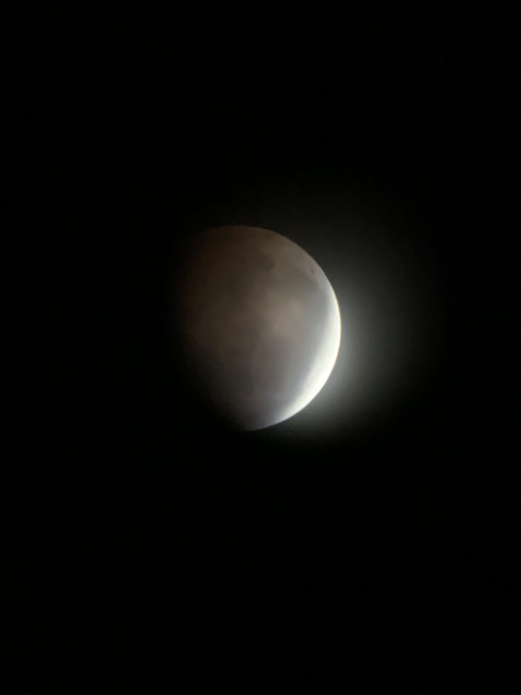 A crescent moon glowing gold in the dark during an eclipse